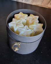 Load image into Gallery viewer, photo of a jar of wax melts, the jard is black carbaord in matt black, the wax melts are star shape with a covering of light coloured glitter, arranged 15 melts to a jar 5 melts in each layer arranged in a circular fashion

